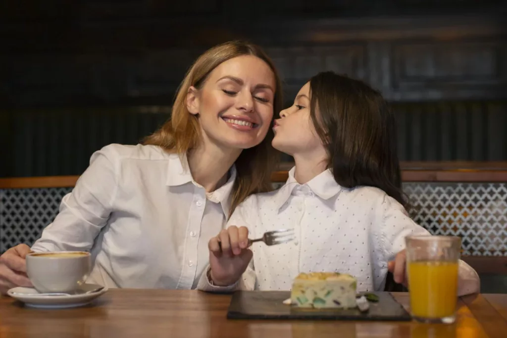 Filha criança beijando a mãe enquanto seprepara para comer um pedaço de torta.