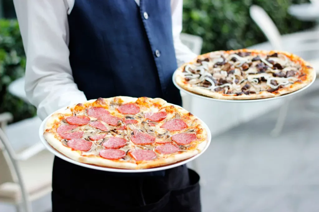 Garçom segurando duas pizzas de sabores diferentes nas mãos.