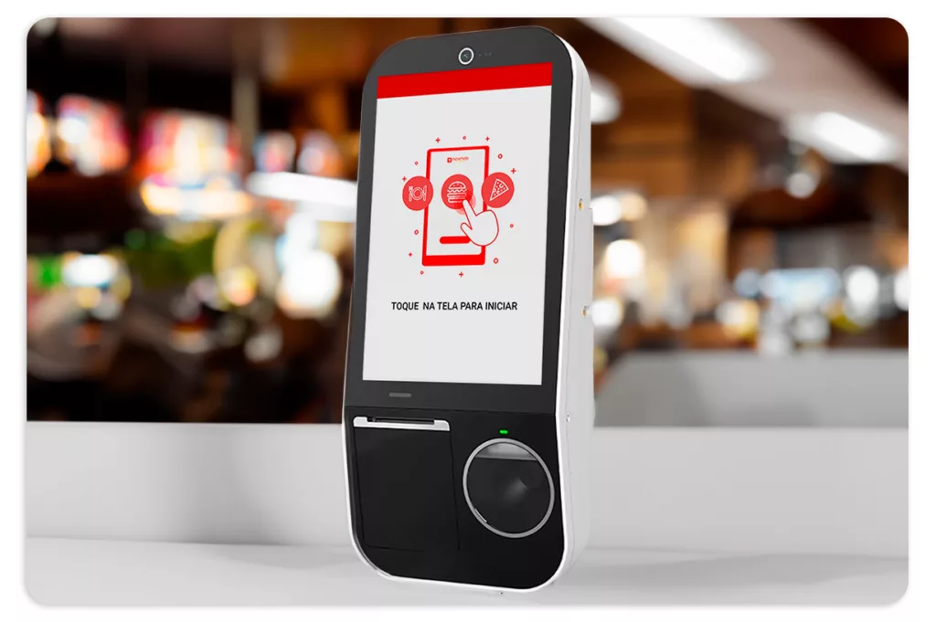 Imagem do aparelho Smart Kiosk. Na tela da maquininha encontra-se a página inicial do aplicativo.